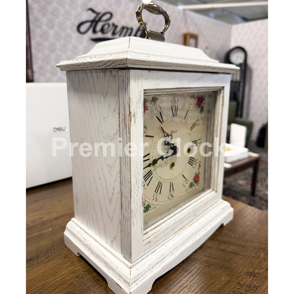 Hermle Austen Mechanical Mantel Clock in White real photo of a white distressed wood mantel clock with a decorative floral clock face and a hanging ring at the top - Premier Clocks